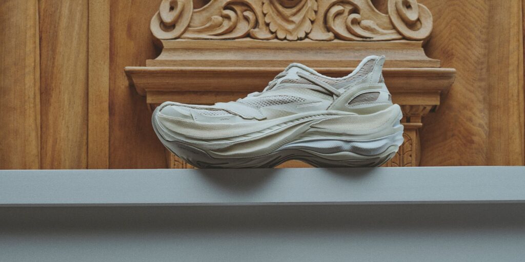 White and beige sneaker with a lot of elegant swoopy lines. Positioned beneath a brown grecco-roman column.