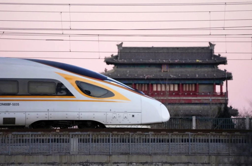 A train speeds past a building with traditional Chinese architecture.