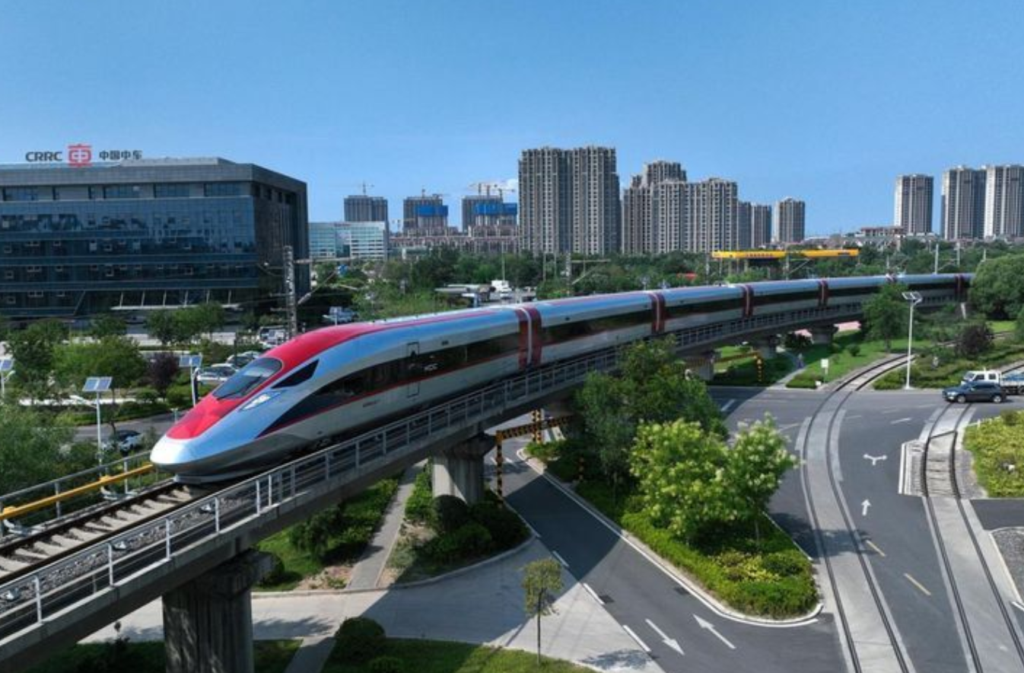 A red and blue train on an elevated track speeds past an urban skyline.