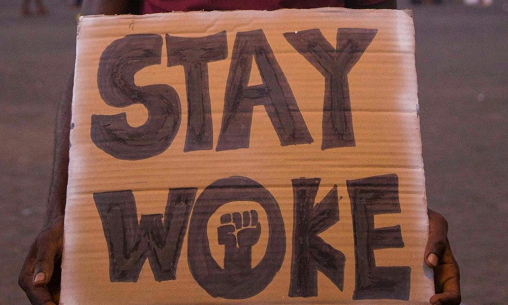 Man Wearing a Hat Holding a Placard with a Text Stay Woke. Photo courtesy of FPD Images on Pexels.