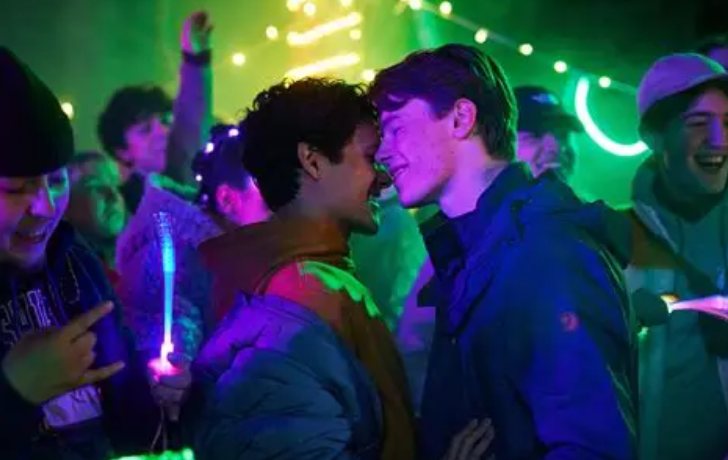 Queer characters from Young Royals looking happy and in love, dancing in a nightclub atmosphere.