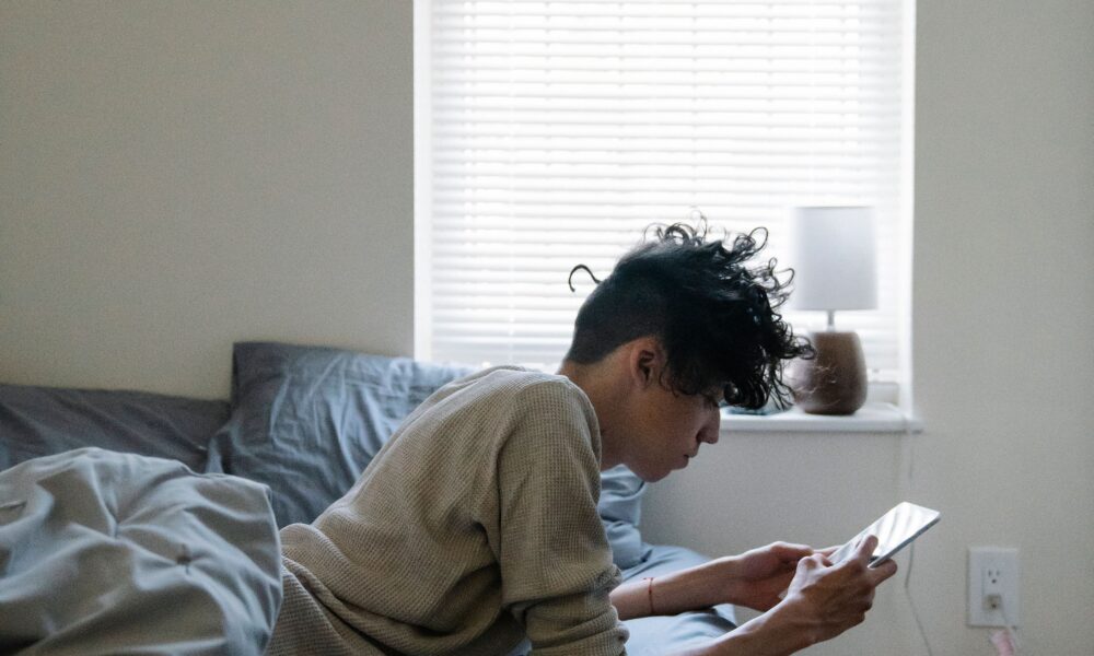 Teen boy sitting on his bed looking at his smartphone.