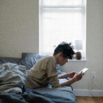 Teen boy sitting on his bed looking at his smartphone.