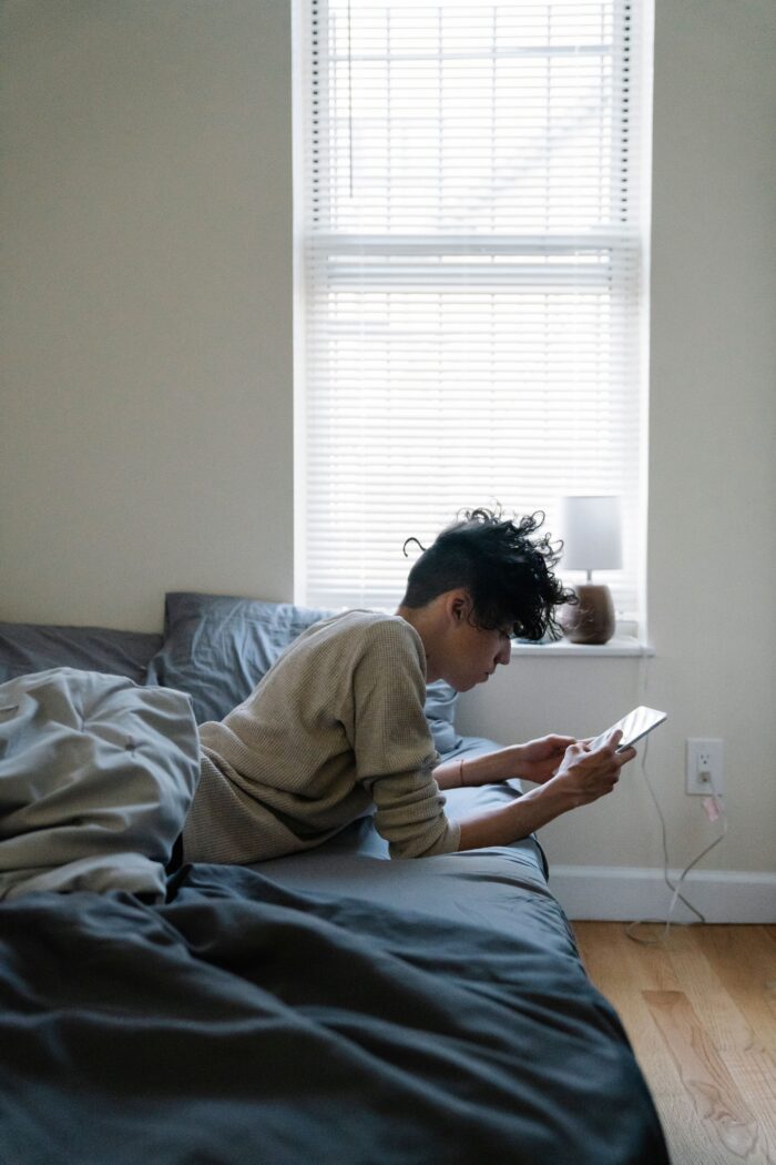 Teen boy sitting on his bed looking at his smartphone.