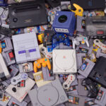 Photo of several retro gaming consoles and game cartridges in a scattered pile